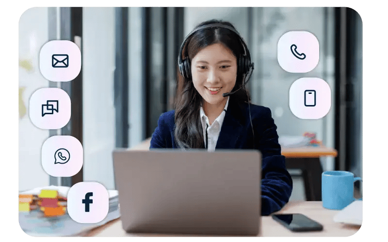 Woman at a laptop with a headset showing all of the different communications channels around her that she's able to support, they include, email, text, whatsapp, facebook, and telephone