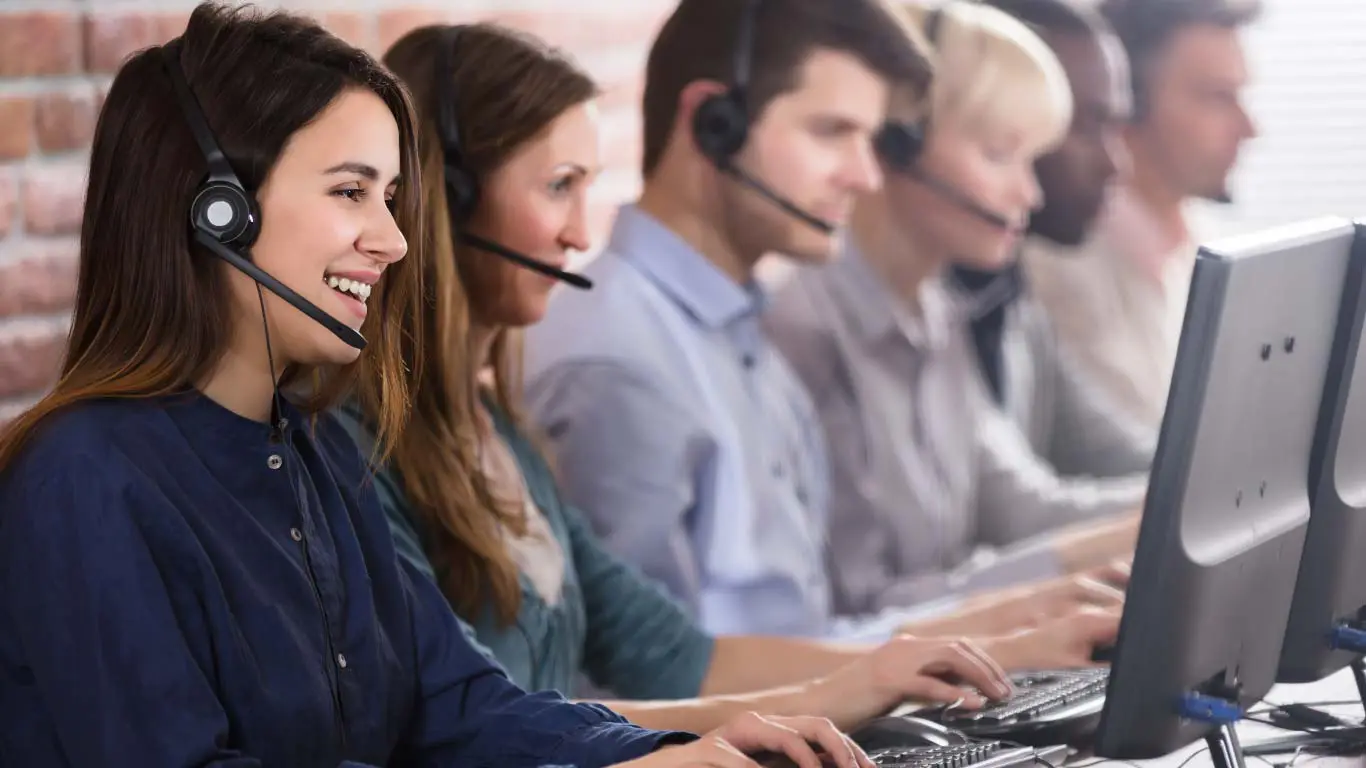 Fila de agentes trabalhando usando fones de ouvido e monitores